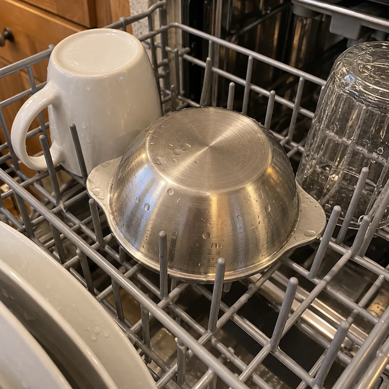 The bowl upside down on the top rack of a dishwasher, between a mug and a glass